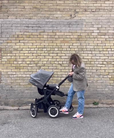 Mom pushing the brake on the best stroller in front of a brick wall