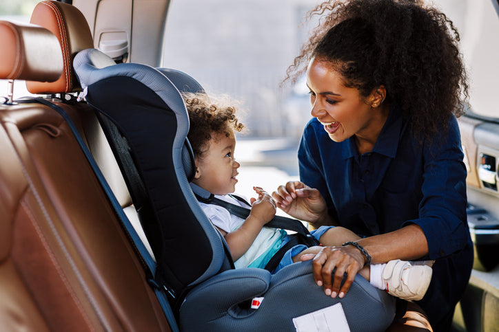 Smiling young mom putting her baby in the best car seat with the door open