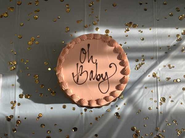 A chocolate cake with the words “Oh Baby” on a confetti background and other baby shower trends