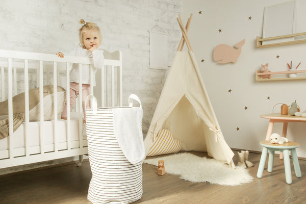 Toddler girl standing in her crib in a decorated nursery room with nursery items