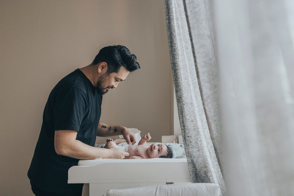 Father changing baby’s diaper on a diaper changing table next to nursery items