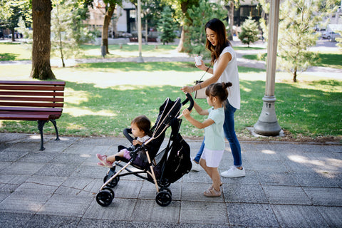 Mom and daughter pushing baby in a foldable stroller in the park