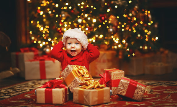Happy baby in a Santa hat sitting in front of a Christmas tree with baby items on sale