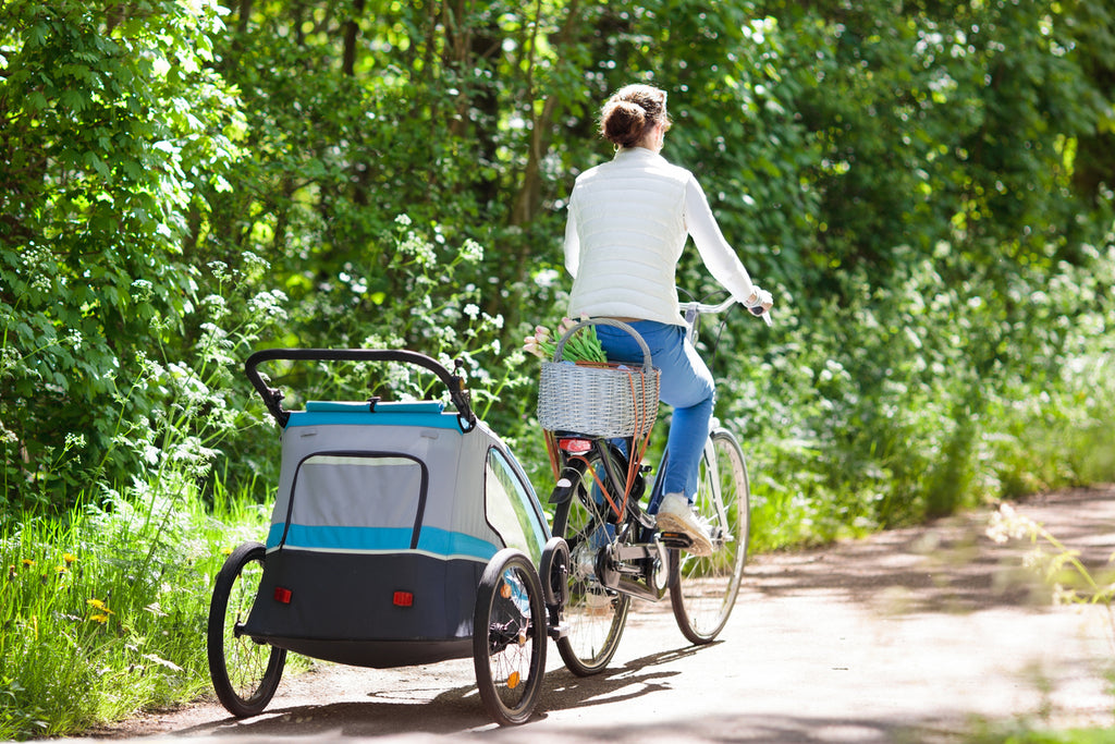 Mother riding a bicycle with a bike trailer attached on a paved path in the forest