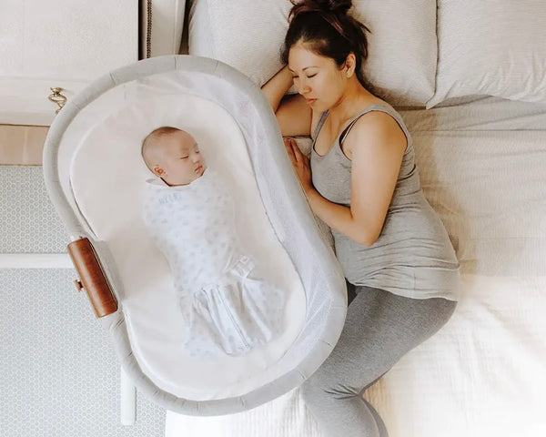 Sleeping NYC mom lying next to a Halo Bassinet baby item where her baby is swaddled and sleeping