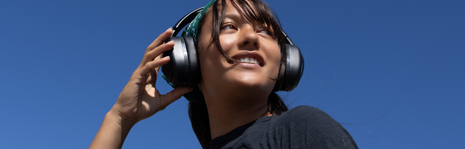 A smiling woman, facing left and wearing TWT Audio's REVO wireless TW340 headphones, adjusts the sound settings.