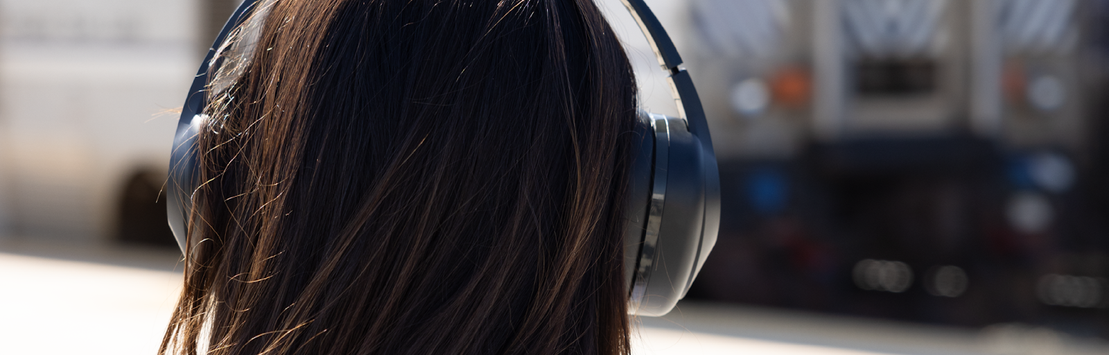 A woman wearing TW340 headphones from TWT Audio gazes at an approaching subway train, immersed in her music and seemingly detached from her surroundings.