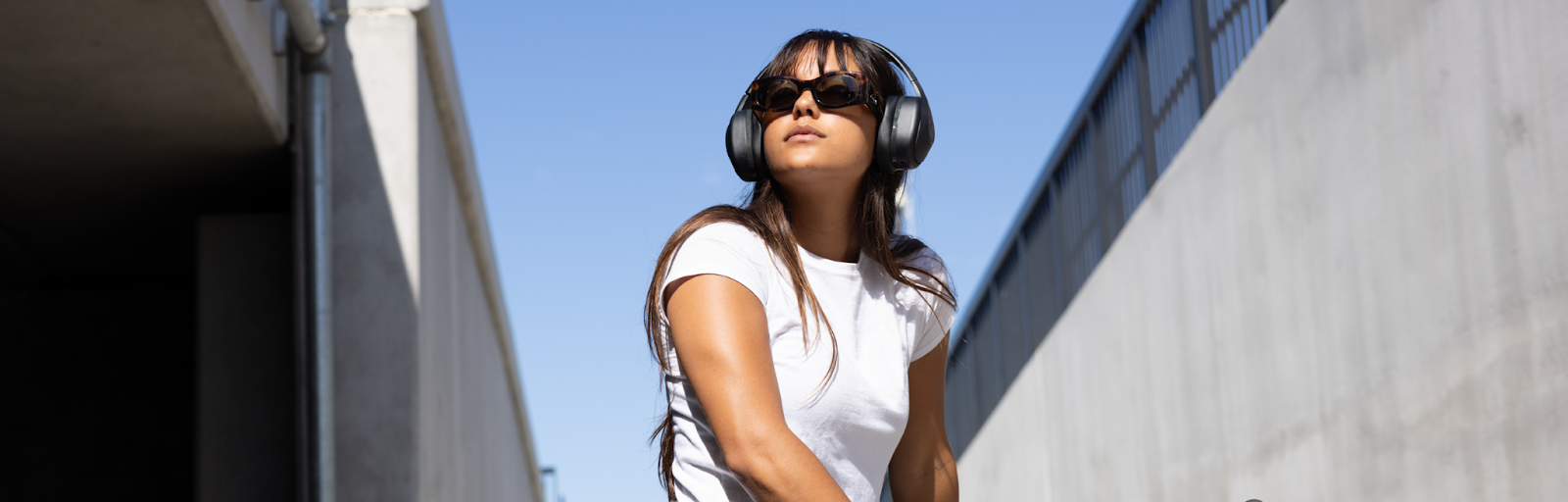 : A woman wearing TW340 headphones from TWT Audio stands on a sidewalk, enjoying her music while surrounded by the urban environment.