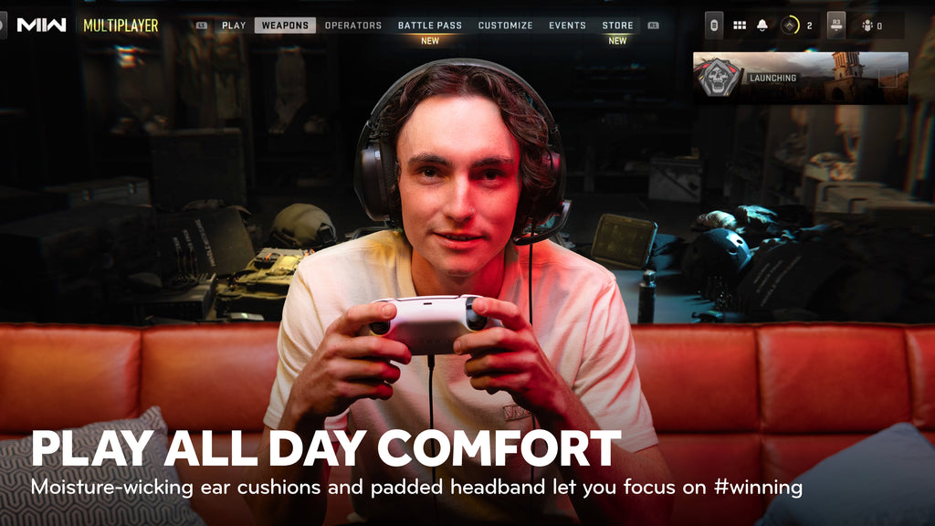 Focused male gamer wearing a headset while holding a controller, with a caption emphasizing 'PLAY ALL DAY COMFORT' and features like moisture-wicking ear cushions for extended gaming sessions.