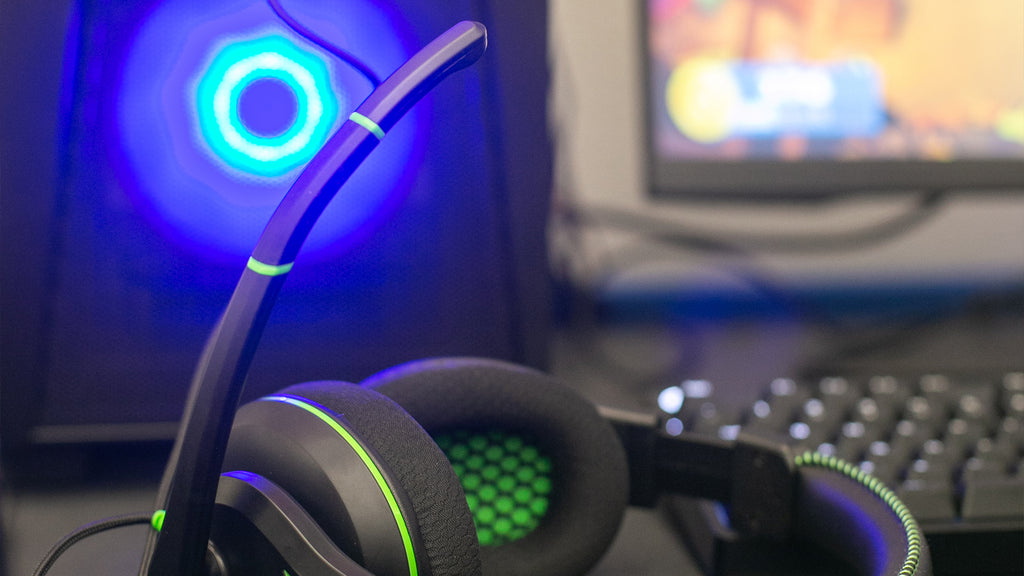 TWT Audio’s 250XG Victory Gaming headset  placed in front of a gaming PC and keyboard on a classroom desk. The headset's microphone is raised, emphasizing its plush ear cushions.