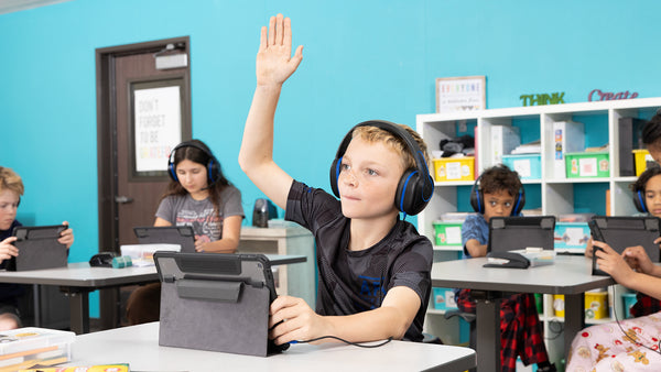 Student in class raising a hand while wearing Revo headphones by TWT Audio and using a classroom tablet