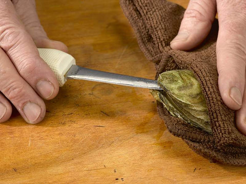 Towel over Oyster on Wooden Surface with Oyster Knife Inserted into Oyster