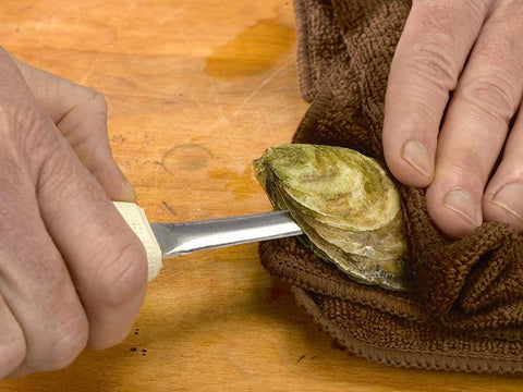 Towel over Oyster on Wooden Surface with Oyster Knife Along Roof of Oyster