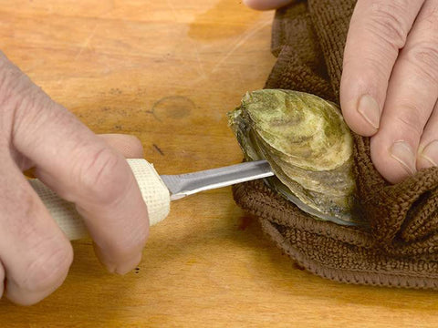 Towel over Oyster on Wooden Surface with Oyster Knife Separating Shells