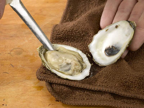 Oyster Opened on Wooden Surface Towel and Oyster Knife in Hand