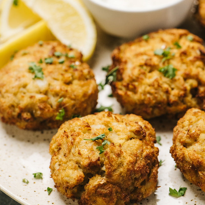 Close Up of Crab Cakes and Lemon Wedges on White Plate