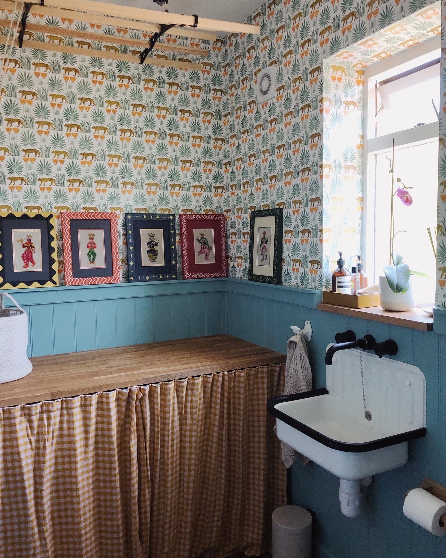 Blue washroom with ceramic sink and Lioness & Palms tropical wallpaper on the walls