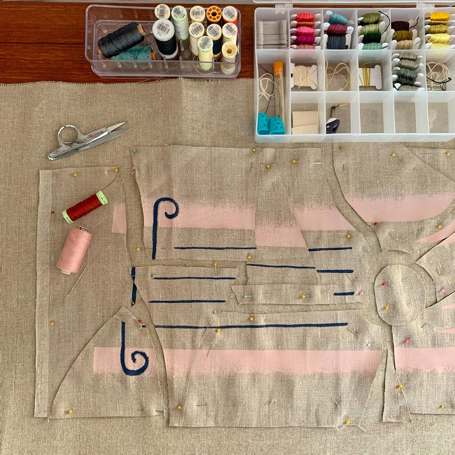 Work in progress photo of artist creating a hand-sewn wallhanging, featuring needles, spools of thread, and scissors