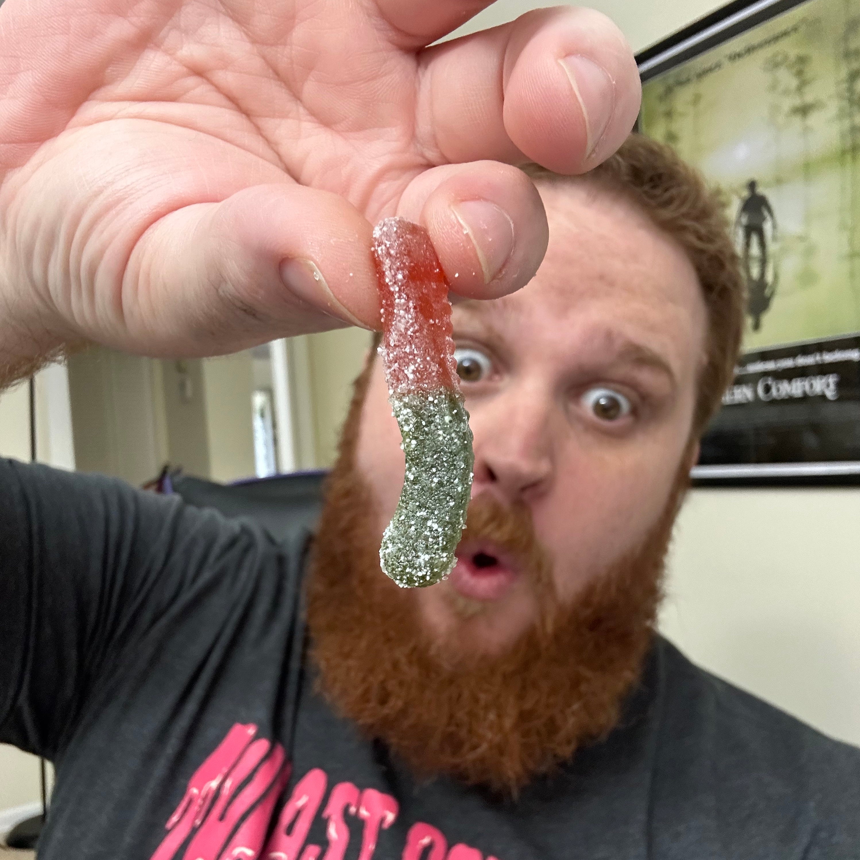 Man holding a sour gummy worm with a surprised expression.