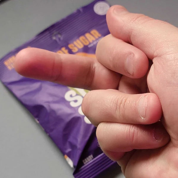 Close-up of a hand with crossed fingers, background partially showing a purple sugar packet.