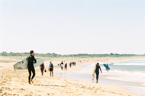 Group of surfers carrying surfboards along the shoreline