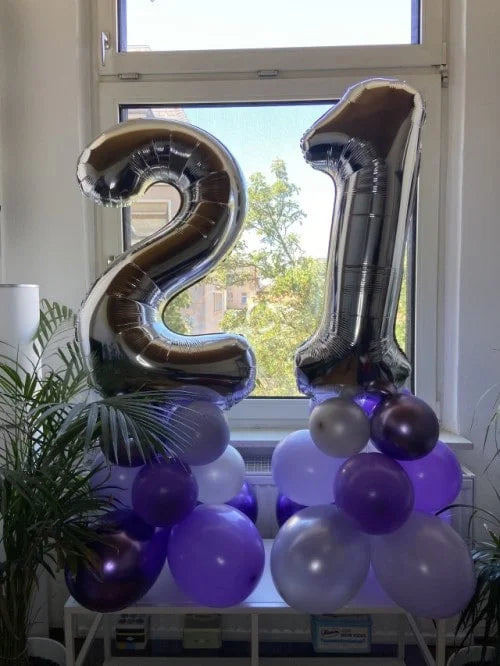 Ballontürme mit den Zahlen 2 und 9 aus Latexballons in Lila und Weiß und XXL Zahlenballons in Silber vor einem Fenster