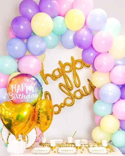 Bunte Geburtstagsdeko in den Farben Gelb, Lila, Rosa, Türkis, und Blau, mit Ballongirlande, 'Happy B-Day' Ballonschriftzug, 'Happy Birthday' Folienballon, und gold-weißer Tischdekoration