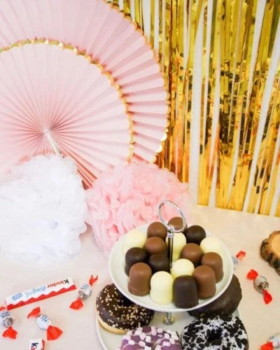Candybar mit mini Dickmans, Donuts, Kinderriegel und Schokobons, rosa Fächern mit goldenem Rand, weißen und rosanen Pom Poms, und goldenem Glitzer-Vorhang