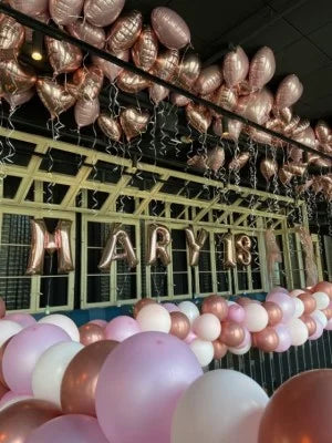 18. Geburtstagsdeko in Rosa und Roségold mit Folienballon-Herzen unter der Decke, einer Ballongirlande und 'Mary 18' XXL Zahlenballons