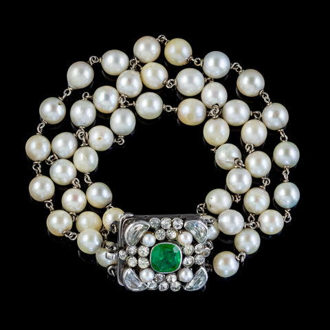 Three-strand pearl bracelet and with a green gem in the centre on a black background