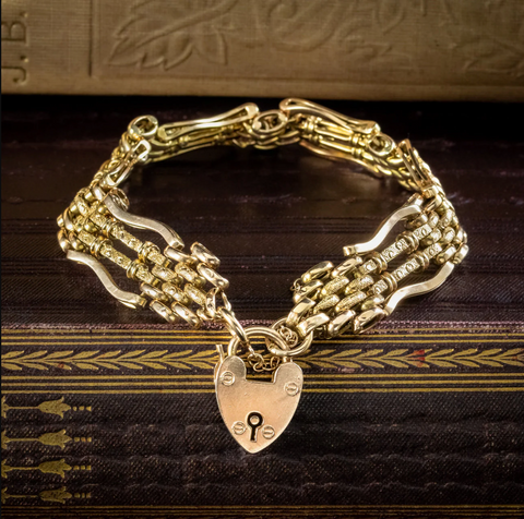 Gold gate chain bracelet with heart padlock resting on a leather-bound book