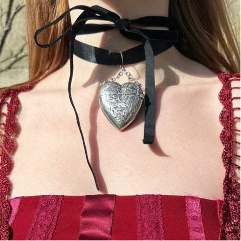 Silver heart locket worn on the neck with a black ribbon 