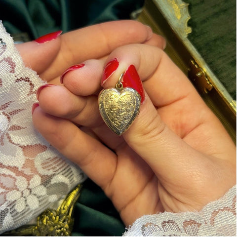 Small heart locket held in hand with red nails