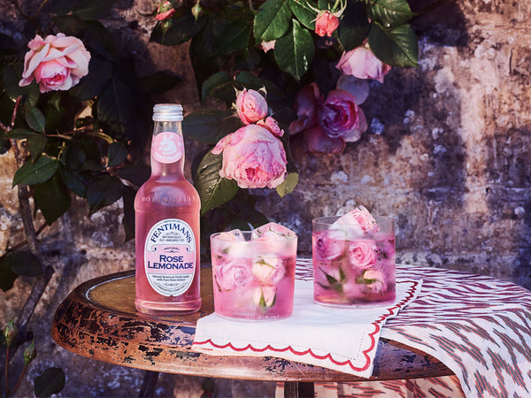 Fentimans Rose Lemonade on a table in front of a pink rose plant