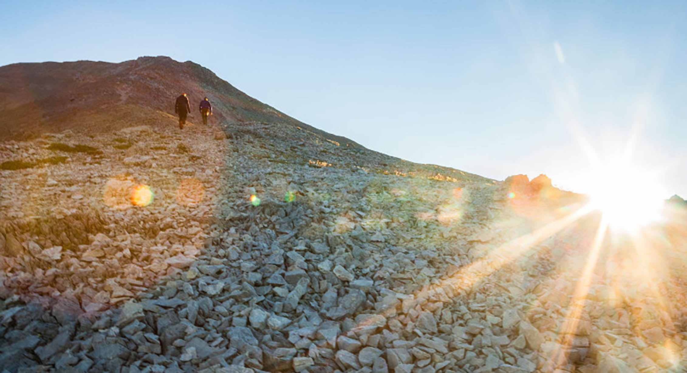 two hikers make their way across a scree field