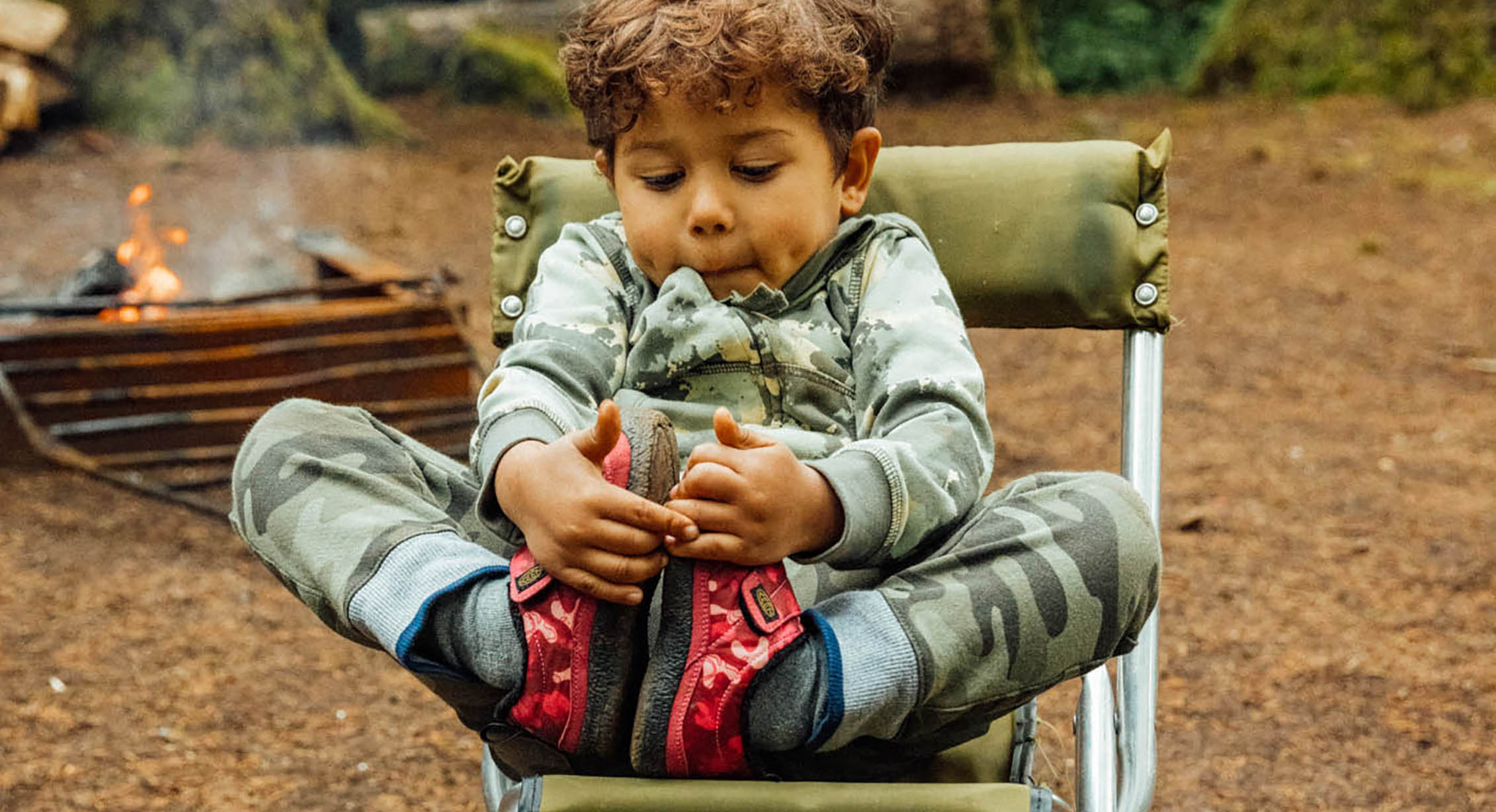 A toddler stretching in a camping chair outside