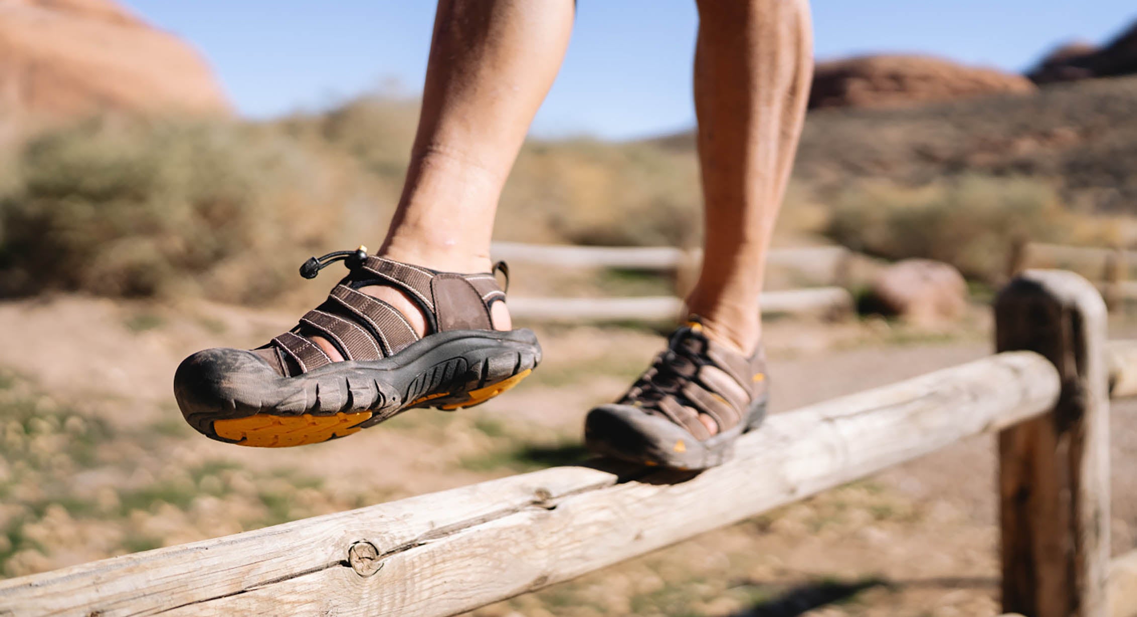 a person wearing a pair of Newport sandals balances on a fence rail