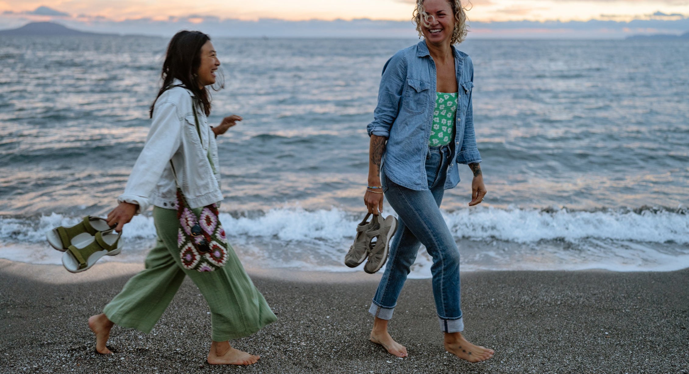 two friends walk barefoot across the beach