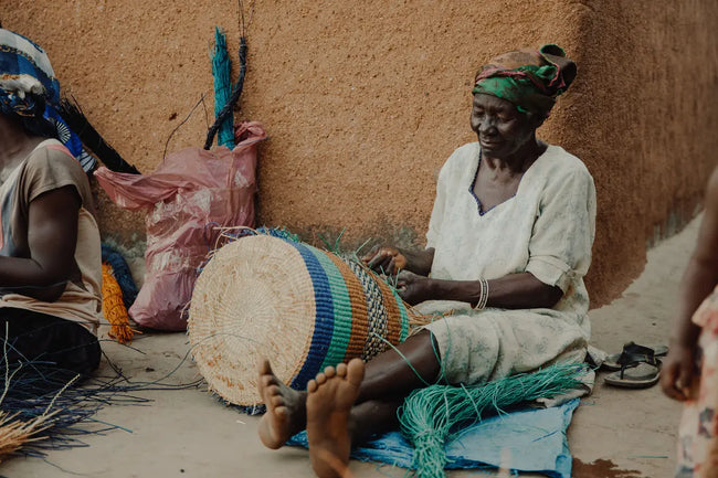 women from Ghana sitting outside and weaves the basket