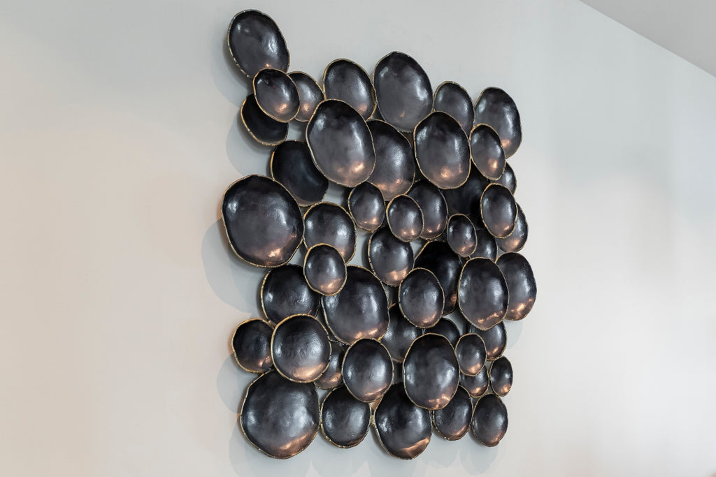 A wall sculpture with black beads arranged in a pile like bubbles.