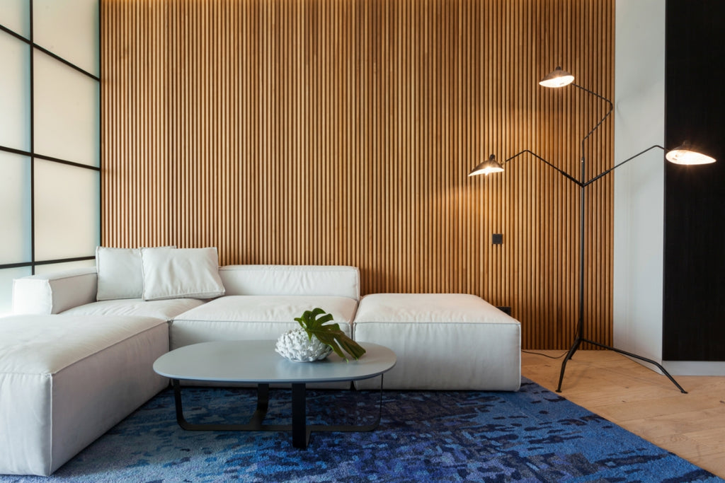 Living room with vertical wood wall paneling with a white couch and blue rug.