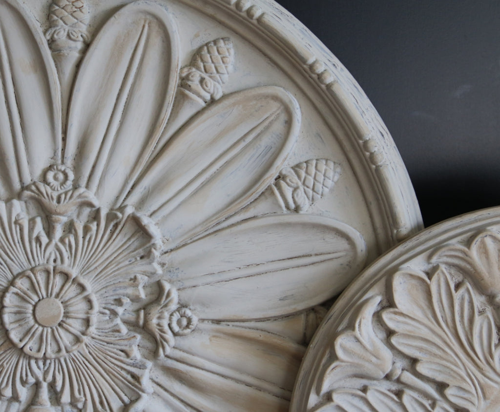 Close up of white ceiling medallions in a circular shape with floral patterns.