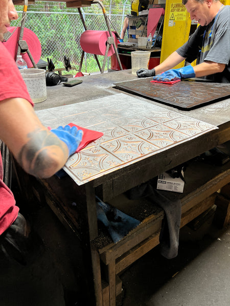 Craftsperson works on a tin tile. 