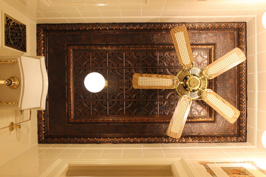 Looking straight up at a small bathroom ceiling with tin tile and a fan.