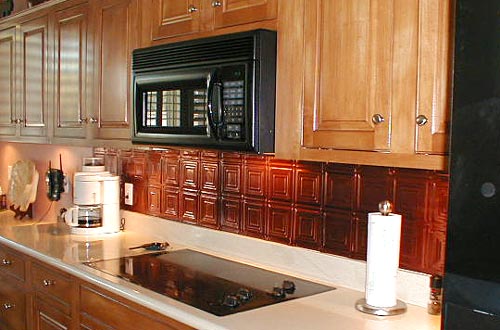 Natural wood cabinets in a kitchen with black appliances and a bronze tin tile backsplash.