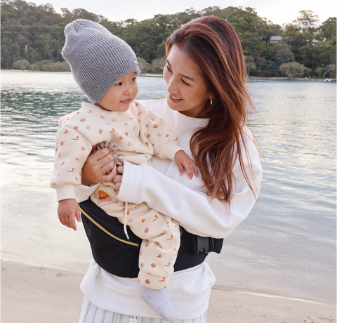 mum carrying child on the beach in winter - best hipseat baby carrier 