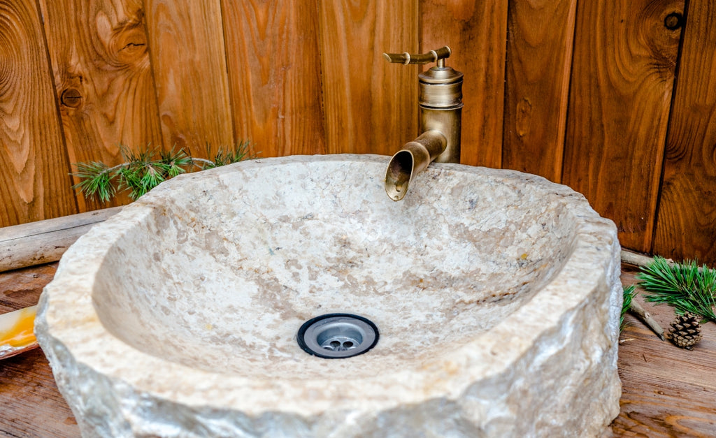 A stone basin sink with a copper faucet.