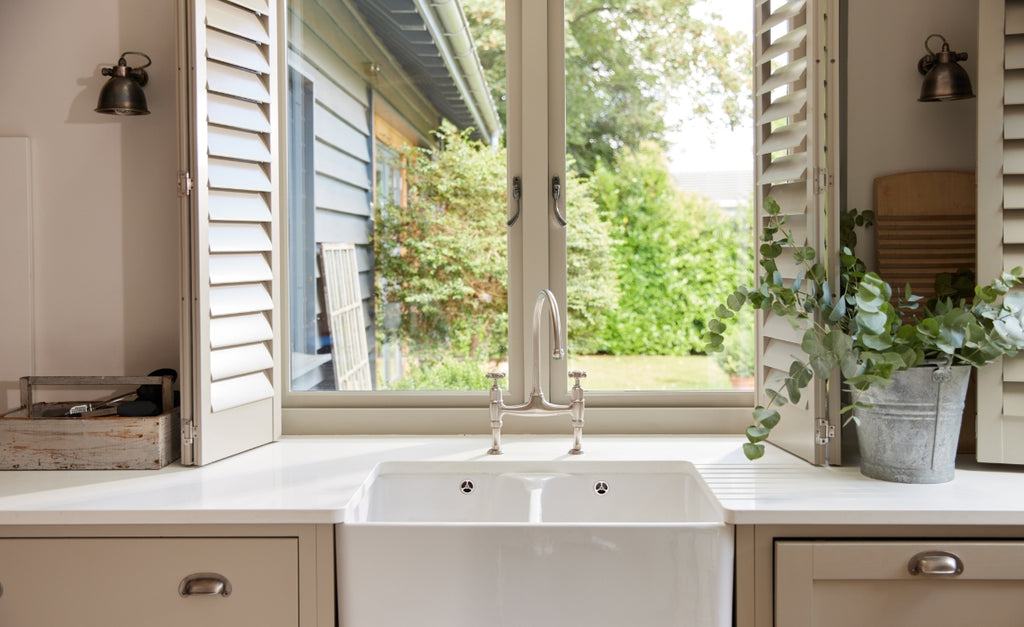 Looking out a window over the kitchen sink with country style shutters in white.