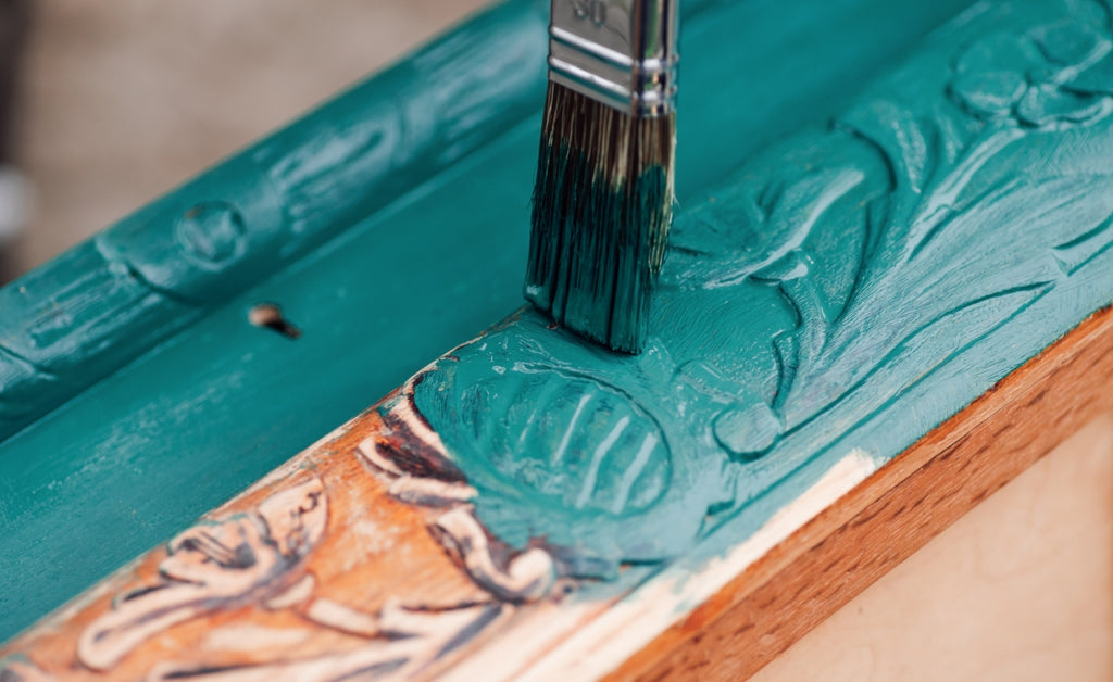 Wood trim with teal paint being applied by a paint brush.