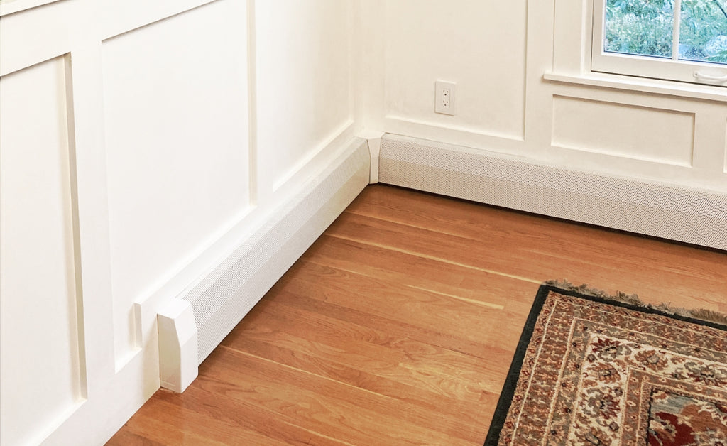 Hydronic baseboard heater in white installed in a corner of a living room.